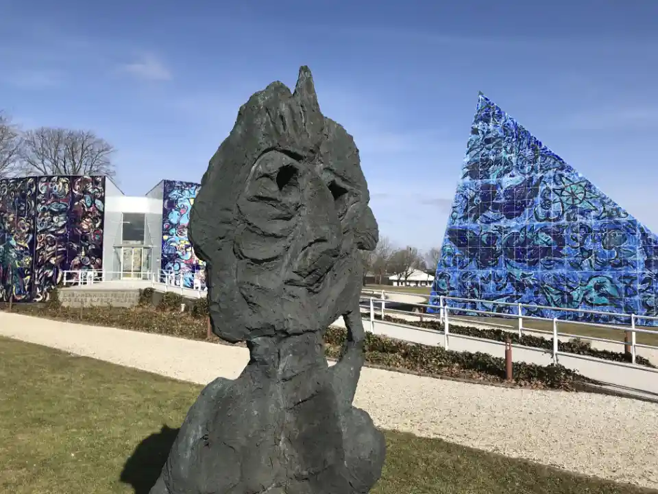 Skulptur af abstrakt ansigt foran farverige mosaikbygninger.