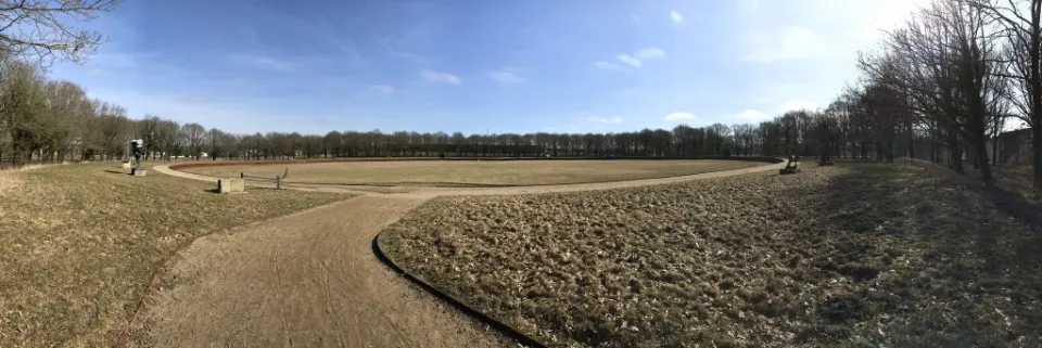 Stor rund græscirkel omgivet af stier og træer.