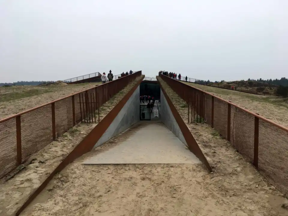 Indgang til underjordisk museum med rustne metalvægge og betonrampe.