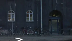 Sort bygning med hvide vinduer og parkerede cykler foran.