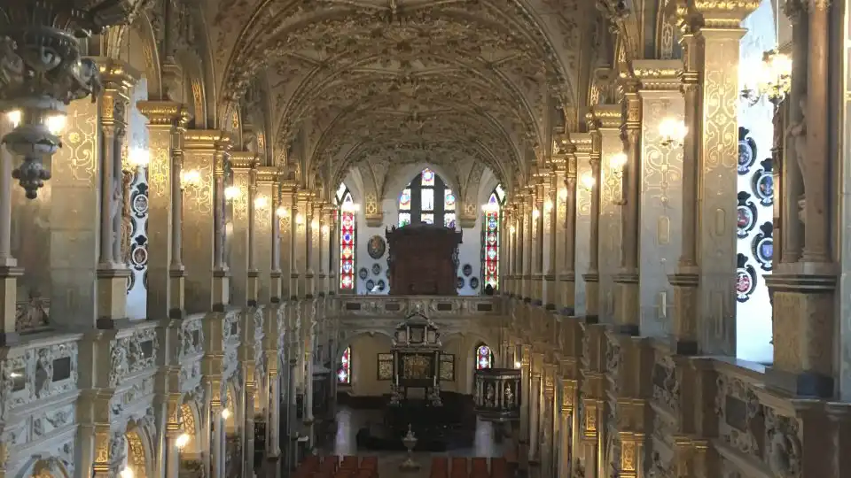 Indre af en overdådigt udsmykket kirke med gyldne detaljer, buet loft og farvede glasvinduer.