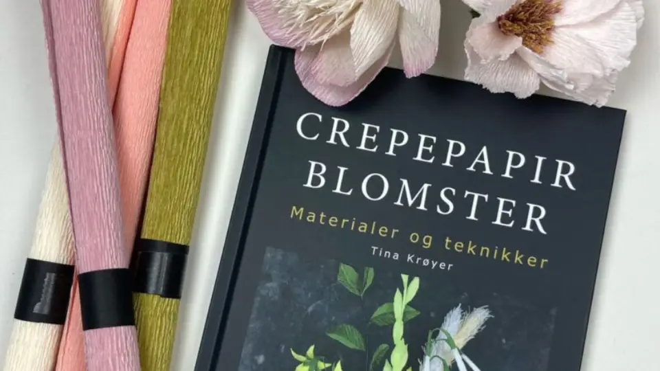 Bogen "Crepepapir Blomster" af Tina Krøyer omgivet af farverigt crepepapir og kunstige blomster.