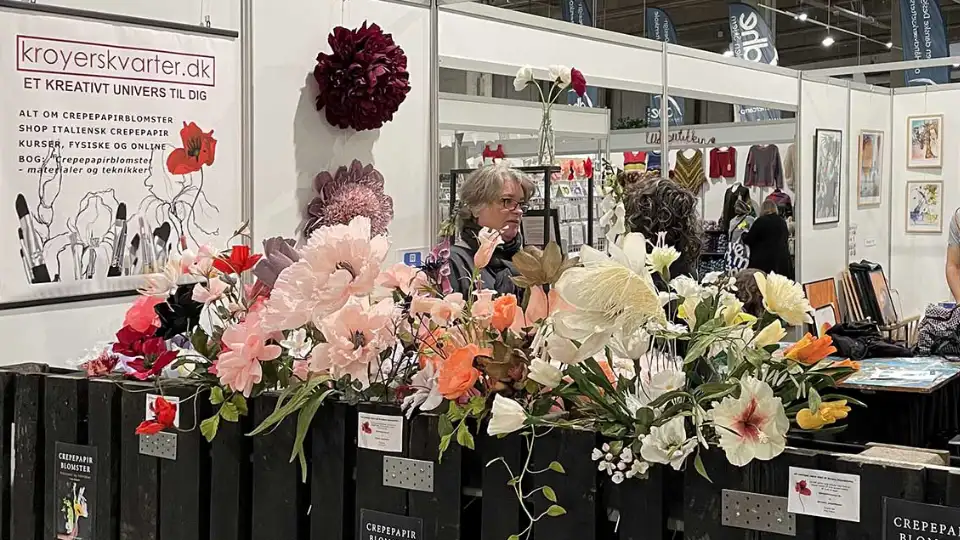 Udstilling af crepepapirblomster på en messe med en kvinde bag standen.