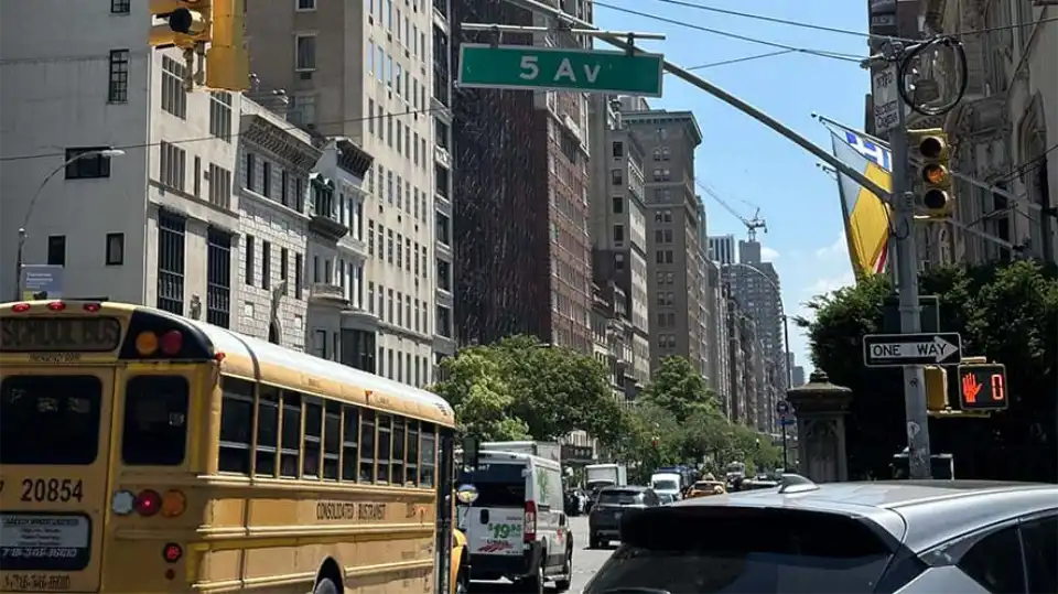 En gul skolebus kører langs en travl gade med højhuse på 5th Avenue i New York City