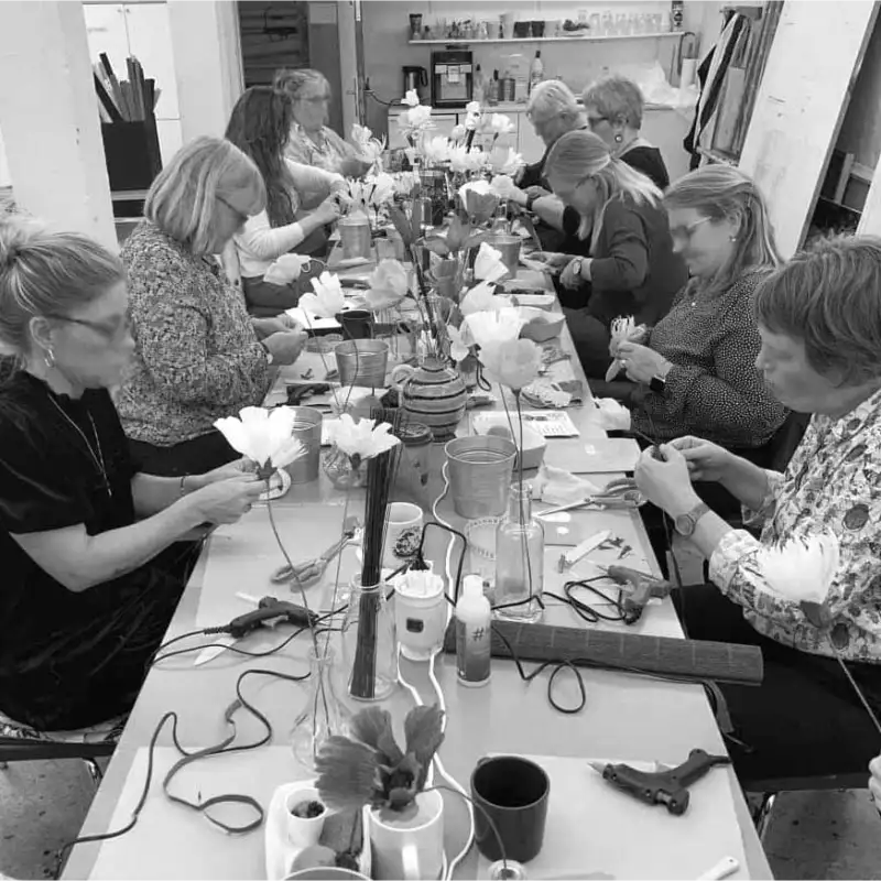 Gruppe af mennesker sidder ved et bord og laver papirblomster